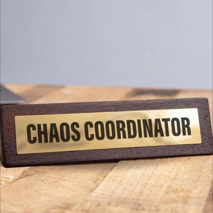 Wooden desk sign with a brass plate reading Chaos Coordinator