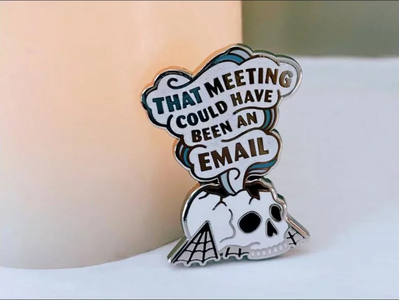 Enamel pin reading That meeting could have been an email above a skull
